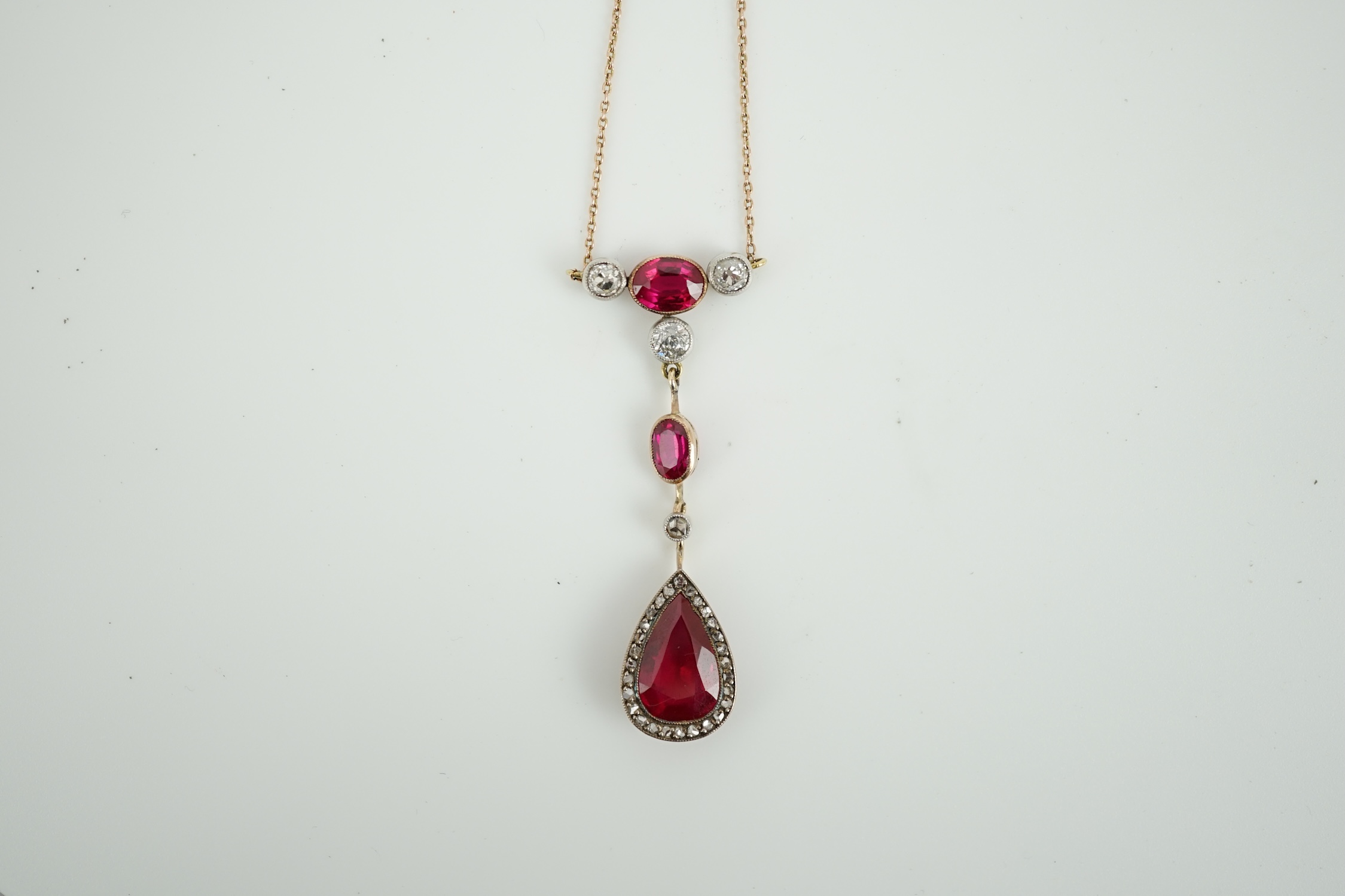 A 9ct, three stone synthetic ruby and four stone diamond set drop pendant necklace, pendant section 49mm, gross weight 5.2 gram.